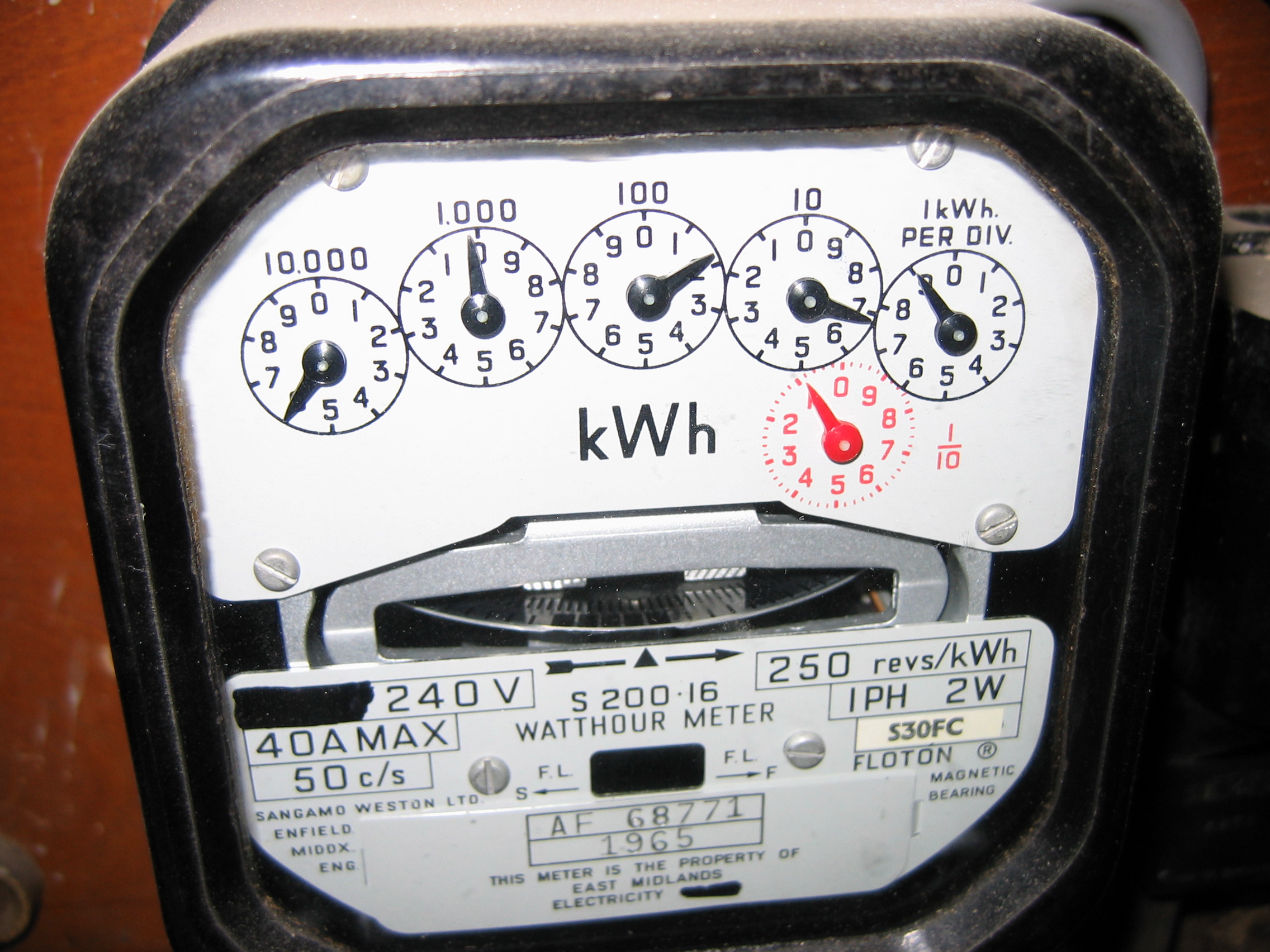 Older electricity meter with five black reading dials and a separate red fractional dial